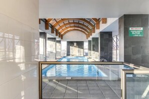 An indoor swimming pool with a glass barrier, a 'NO SACAR' sign, and a view of the cityscape through large windows. - Merced Plaza Apart (Santiago)