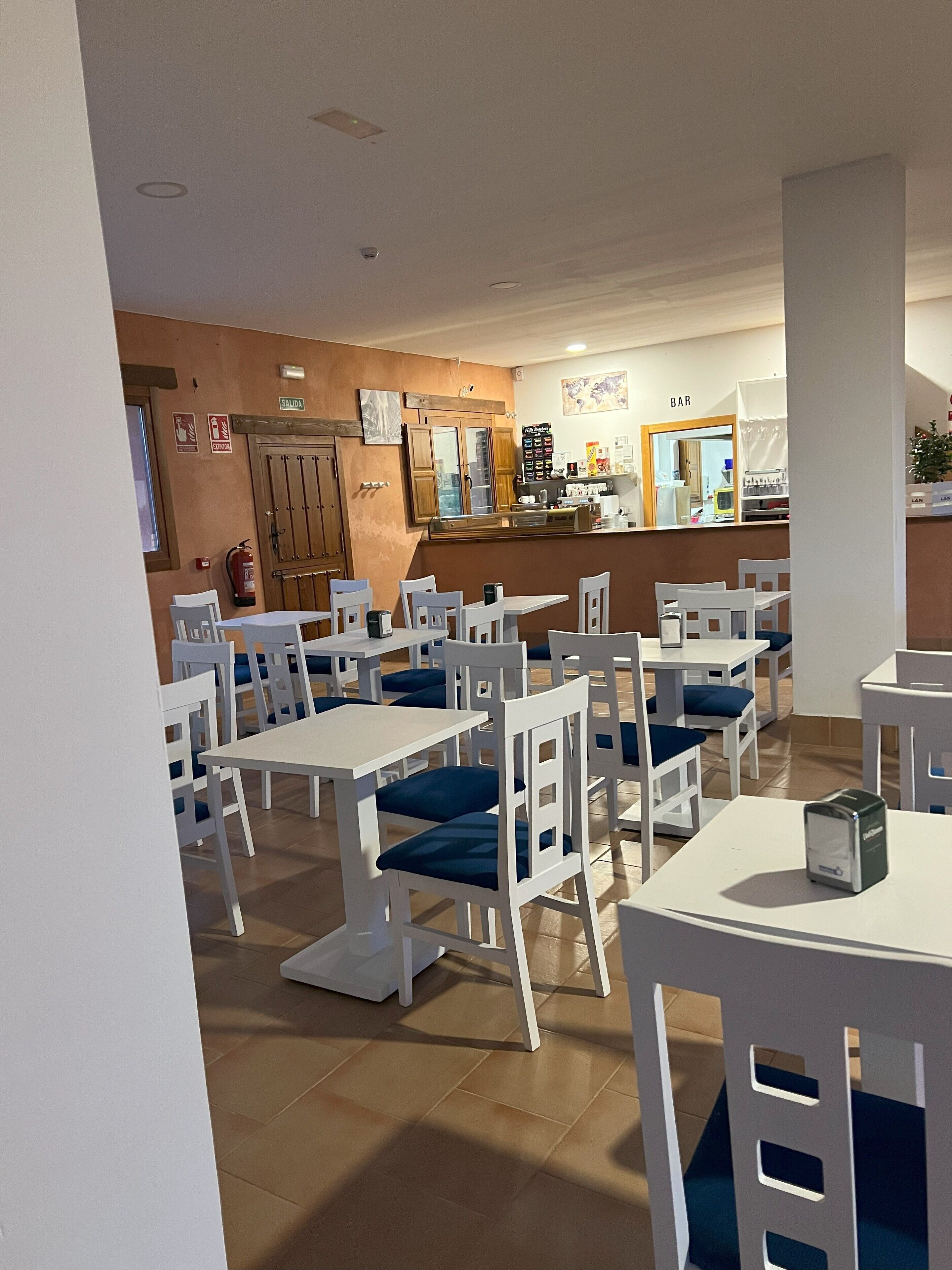 A restaurant with white tables and chairs, a bar area, and a fire extinguisher on the wall.
