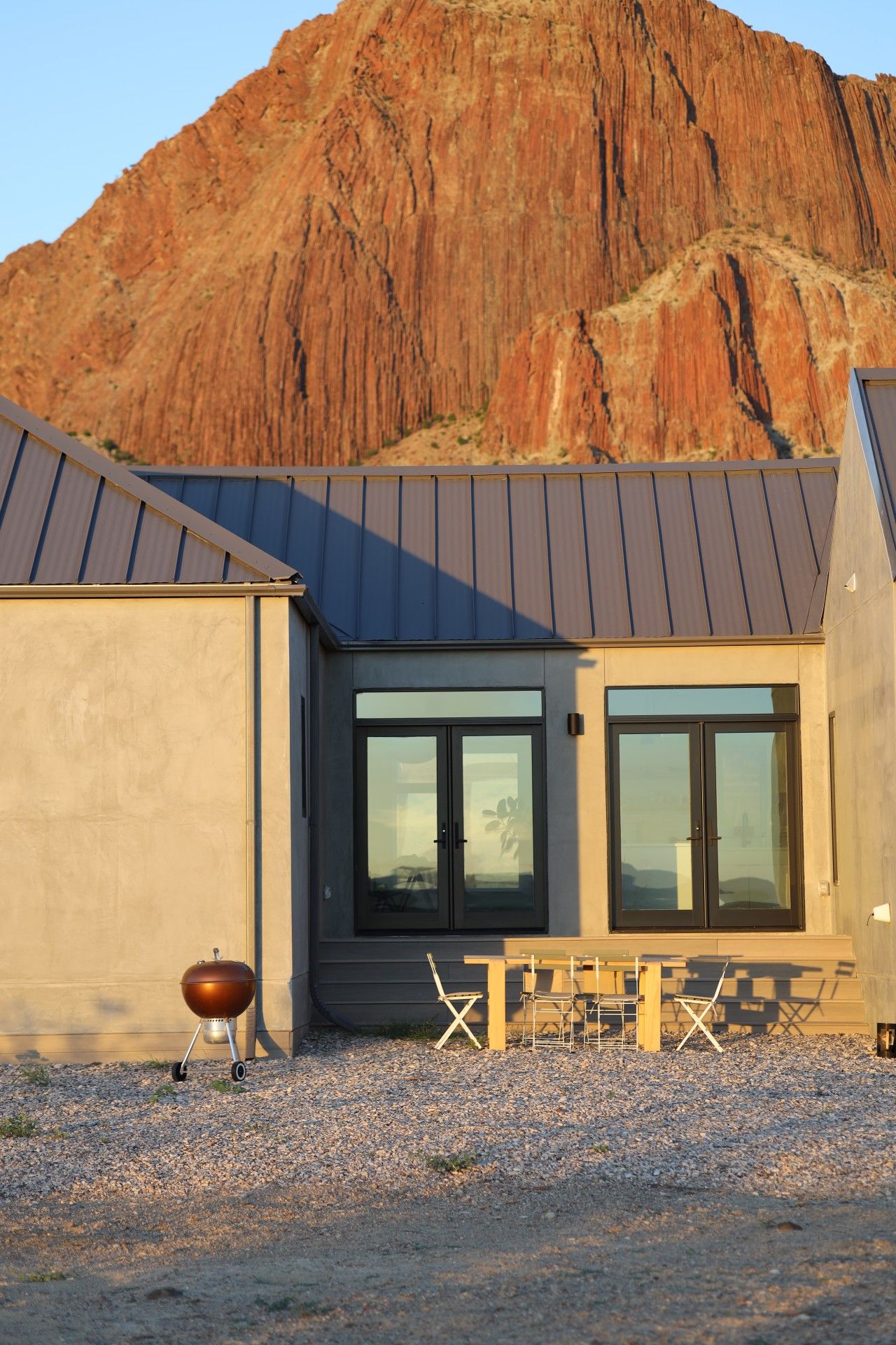 A modern building with a metal roof, large windows, and a barbecue grill in the foreground.