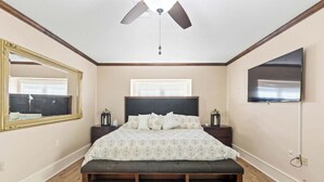 A bedroom with a bed, a ceiling fan, a large mirror, a television, and a window with blinds. - Newly Renovated "Home Away From Home"
A spacious, modernized 4-bedroom home. (Brighton)