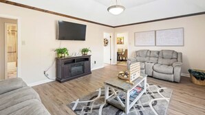 A living room with a grey sofa, a dark entertainment unit, a flat-screen TV, and a patterned rug. - Newly Renovated "Home Away From Home"
A spacious, modernized 4-bedroom home. (Brighton)