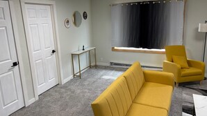 A room with a yellow sofa, a small table, a mirror, and a window with curtains. - Quick Escape 2 Bedrooms n Lingle, Wy! with free Wifi & Parking (Lingle)