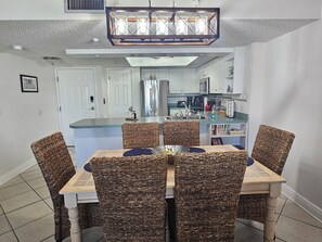 A dining area with wicker chairs, a wooden table, and a kitchen in the background.