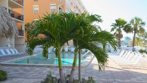 A swimming pool surrounded by lounge chairs, palm trees, and a building with balconies. - Beach Condo at John's Pass (Madeira Beach)