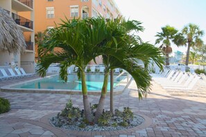Una piscina rodeada de sillones de descanso, palmeras y un edificio con balcones.