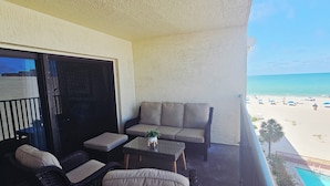 A balcony with wicker furniture, a small table, and a view of the beach. - Beach Condo at John's Pass (Madeira Beach)