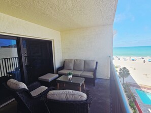 A balcony with wicker furniture, a small table, and a view of the beach.