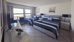 A hotel room with two beds, a TV, a small table with a lamp, and a view of the sea through the windows. - Beach Condo at John's Pass (Madeira Beach)