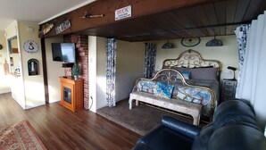 A living room with a fireplace, a television, a bench, and a bed with a headboard.
