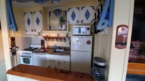 A compact kitchen with white cabinets, a stove, a microwave, and a coffee maker.