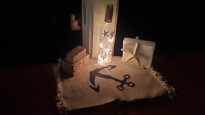 A table with a bottle, a candle, and a small decorative item on a tablecloth with an anchor design.