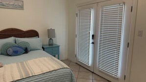 A bedroom with a bed, pillows, a nightstand, a lamp, and a door with blinds. - 3-bedroom, 1st floor condo in charming South Padre Island, 3 min walk to beach (South Padre Island)