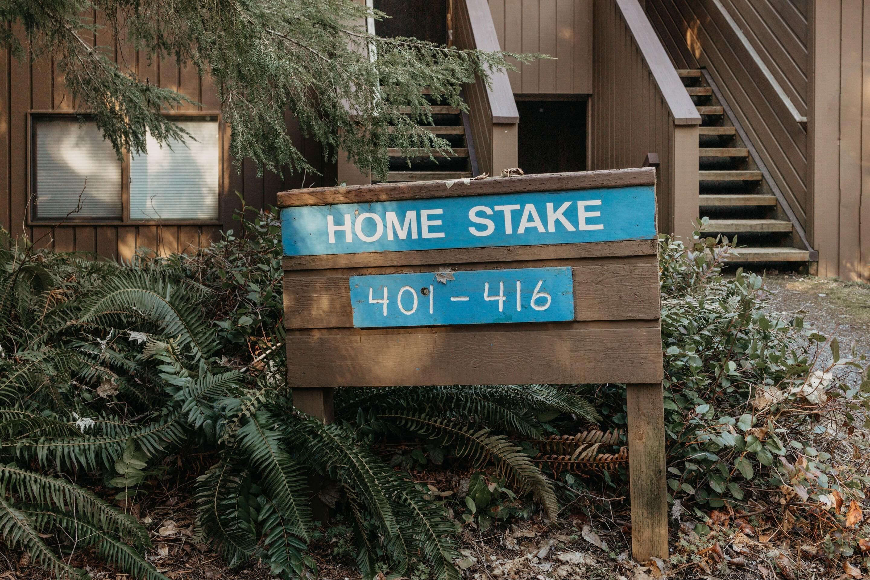A wooden sign with "HOME STAKE" and a phone number "401-416" in front of a building with a staircase.