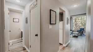 A hallway with a wooden floor, white walls, and a door leading to a room with a window. - Snowater Condo 45sw With a Media Room (Deming)