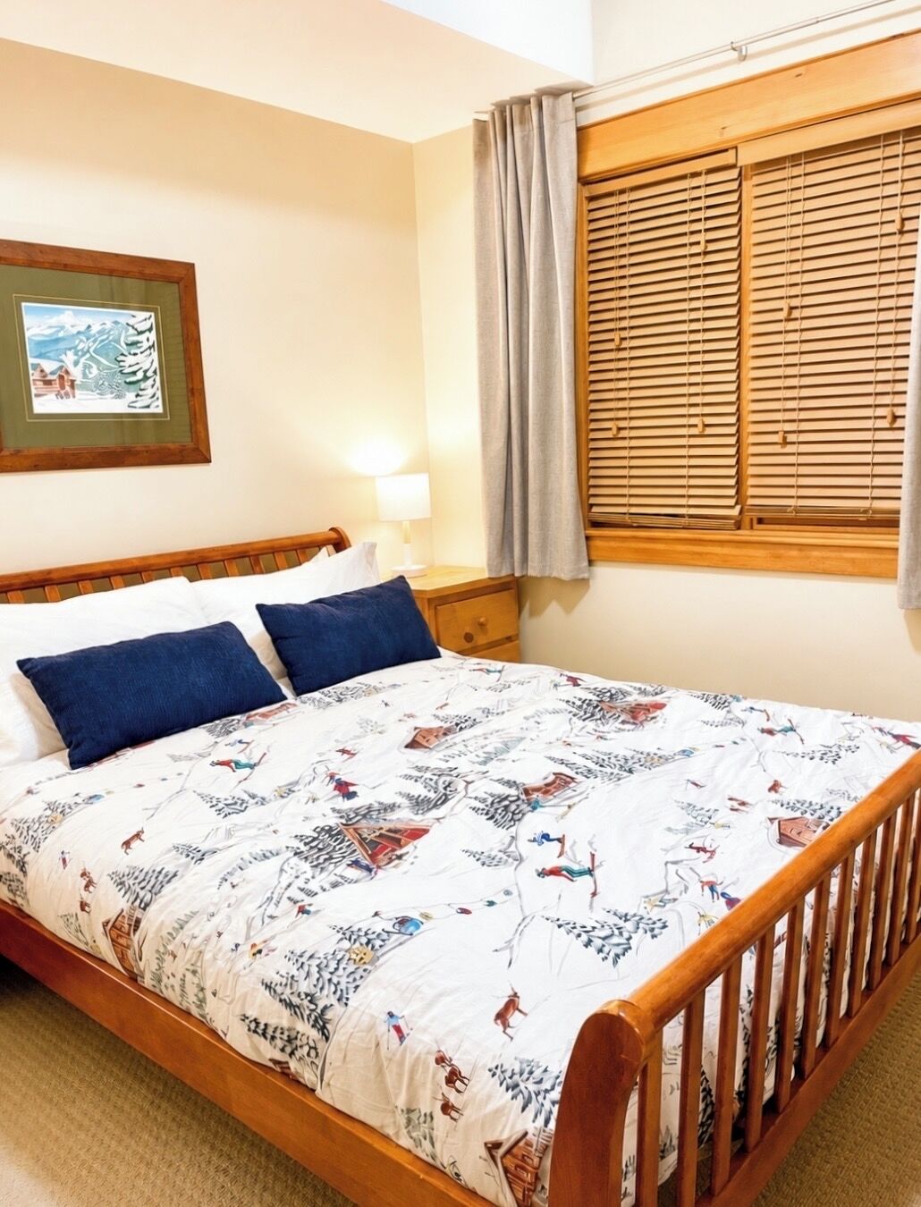 Un lit avec une couvre-lit à motifs, une tête de lit en bois, une table de chevet avec une lampe et une fenêtre avec des volets en bois.