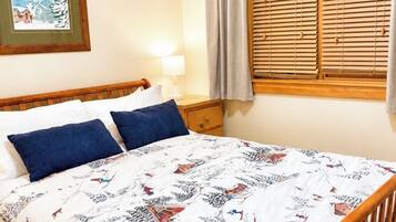 Un lit avec une couvre-lit à motifs, une tête de lit en bois, une table de chevet avec une lampe et une fenêtre avec des volets en bois.