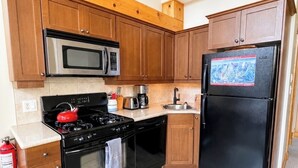 A kitchen with wooden cabinets, a stainless steel microwave, a black stove, a black refrigerator, and a tiled floor. - Red Mtn views, walk to lift, 2 bed, 2 bath condo. Fireplace! (Trail)
