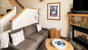 A living room with a sofa, a coffee table, a fireplace, a TV, and a staircase. - Red Mtn views, walk to lift, 2 bed, 2 bath condo. Fireplace! (Trail)