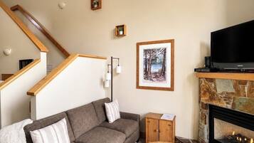 Un salon comprenant un canapé, une table basse, une cheminée, un téléviseur et un escalier.