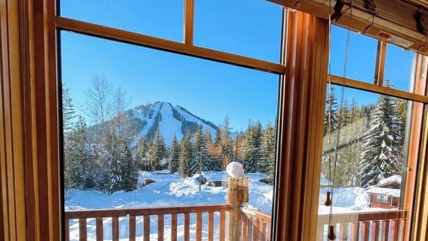 A room with large windows offering a view of a snowy mountain and forest. - Red Mtn views, walk to lift, 2 bed, 2 bath condo. Fireplace! (Trail)