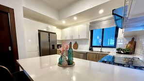 A modern kitchen with white cabinets, a stainless steel refrigerator, a glass island with decorative vases, and a window with a blue view.