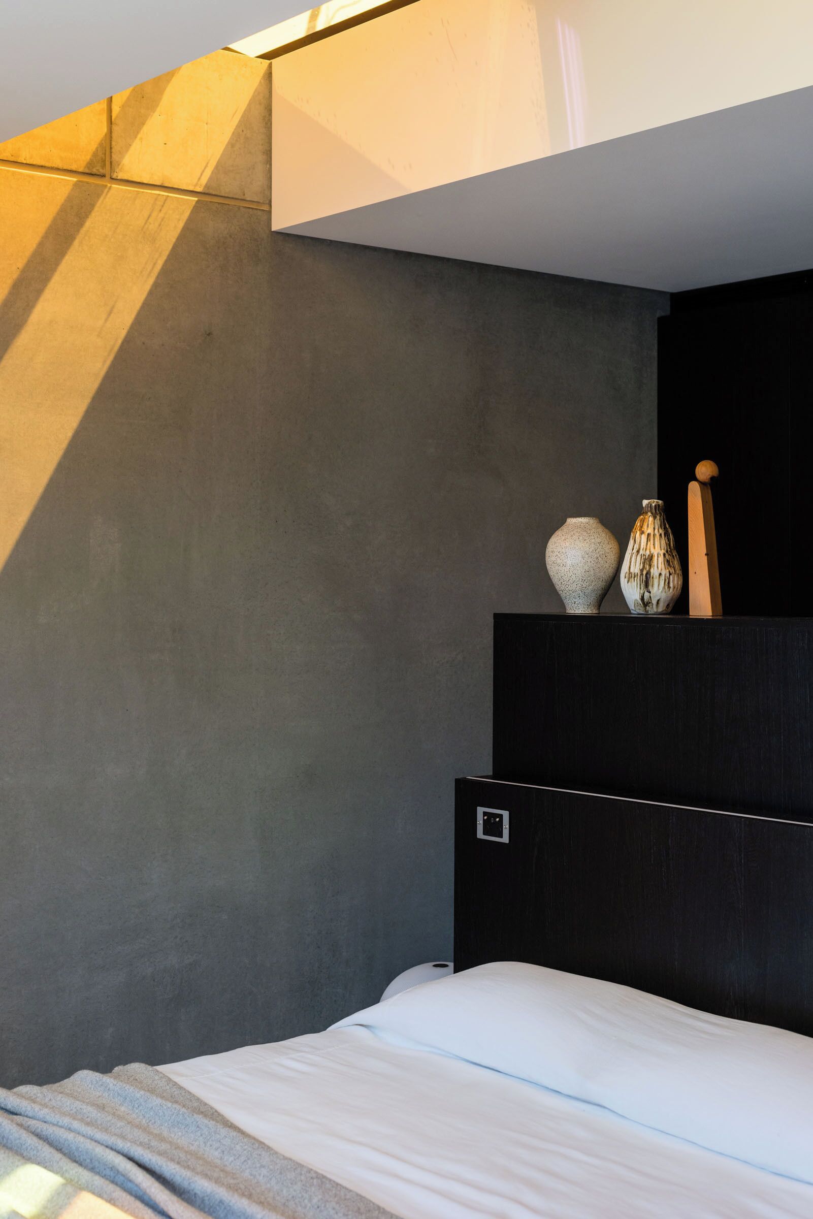 Een moderne slaapkamer met een bed, een nachtkastje en een wandplank met decoratieve objecten.