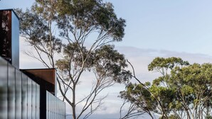 A modern building with a reflective glass facade overlooking a calm body of water and trees. - Vipp Tunnel - Tasmania (Apollo Bay)