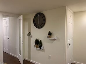 A hallway with white walls, a round wall clock, and three white shelves with small plants. - 1BR, 1BA - 2.5 miles to U.S. Capitol & National Mall (Washington)