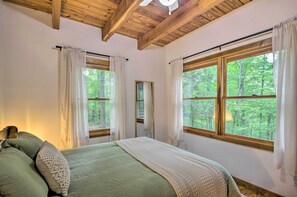 A bedroom with a large bed, wooden beams on the ceiling, and windows with curtains. - the wooder house: charming haven in the woods, family-friendly & dog-friendly (Nellysford)