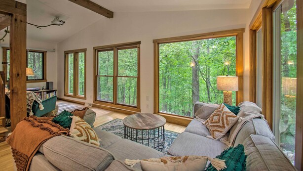 A cozy living room with large windows, a sofa, a coffee table, and a bookshelf. - the wooder house: charming haven in the woods, family-friendly & dog-friendly (Nellysford)