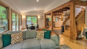 A spacious living room with a large gray sectional sofa, wooden beams, and a staircase leading to an upper level. - the wooder house: charming haven in the woods, family-friendly & dog-friendly (Nellysford)