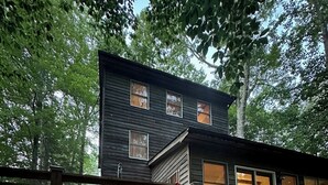 A cabin with a fire pit in the foreground and a deck with chairs. - the wooder house: charming haven in the woods, family-friendly & dog-friendly (Nellysford)