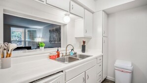 Una cocina moderna con armarios blancos, un lavamanos doble y una ventana con persianas.