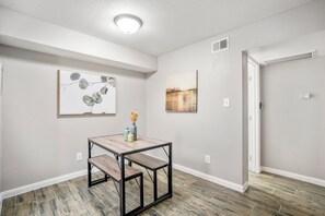A dining area with a wooden table and bench, two wall-mounted paintings, and a door leading to another room. - Towne Plaza Apartments #104 in the Galleria Area (Houston)