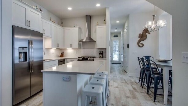 Una cocina moderna con armarios blancos, un refrigerador de acero inoxidable, una isla central con taburetes y una araña.