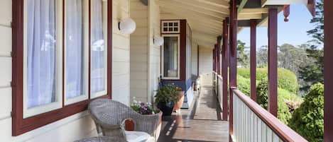 A covered porch with wicker chairs, a potted plant, and a view of greenery.