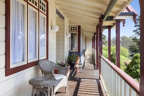 A covered porch with wicker chairs, a potted plant, and a view of greenery.