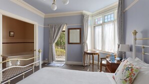 Quarto com uma cama grande, uma cadeira de madeira, uma mesa pequena, um espelho e uma janela com cortinas.