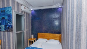 A hotel room with a bed, a nightstand, a wall with a starry pattern, and a door. - dakar International House (Dakar)