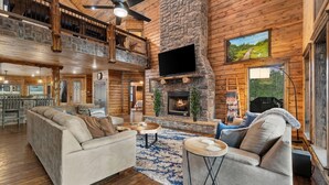 A spacious living area with a fireplace, a large TV, and a high ceiling with exposed beams.