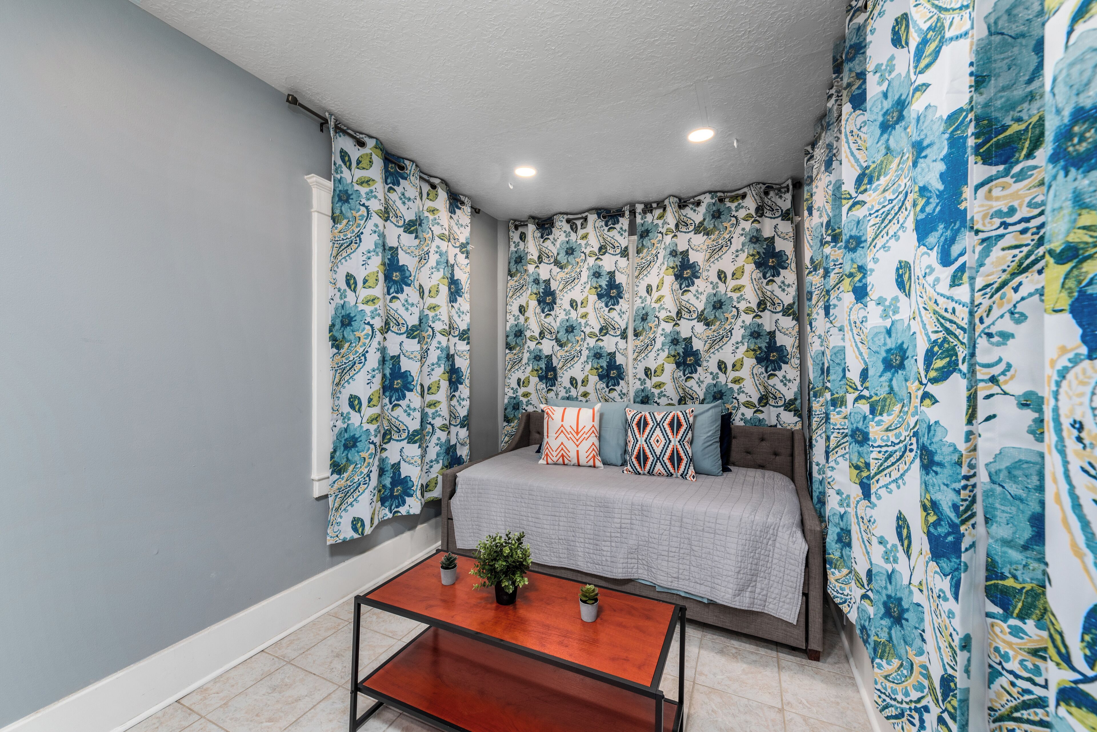Quarto com cama, cortinas, mesa de centro e planta em vaso.