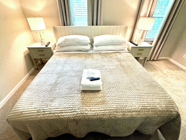 Una cama bien hecha con colcha acolchada, dos mesitas de noche con lámparas y un control remoto sobre la cama.