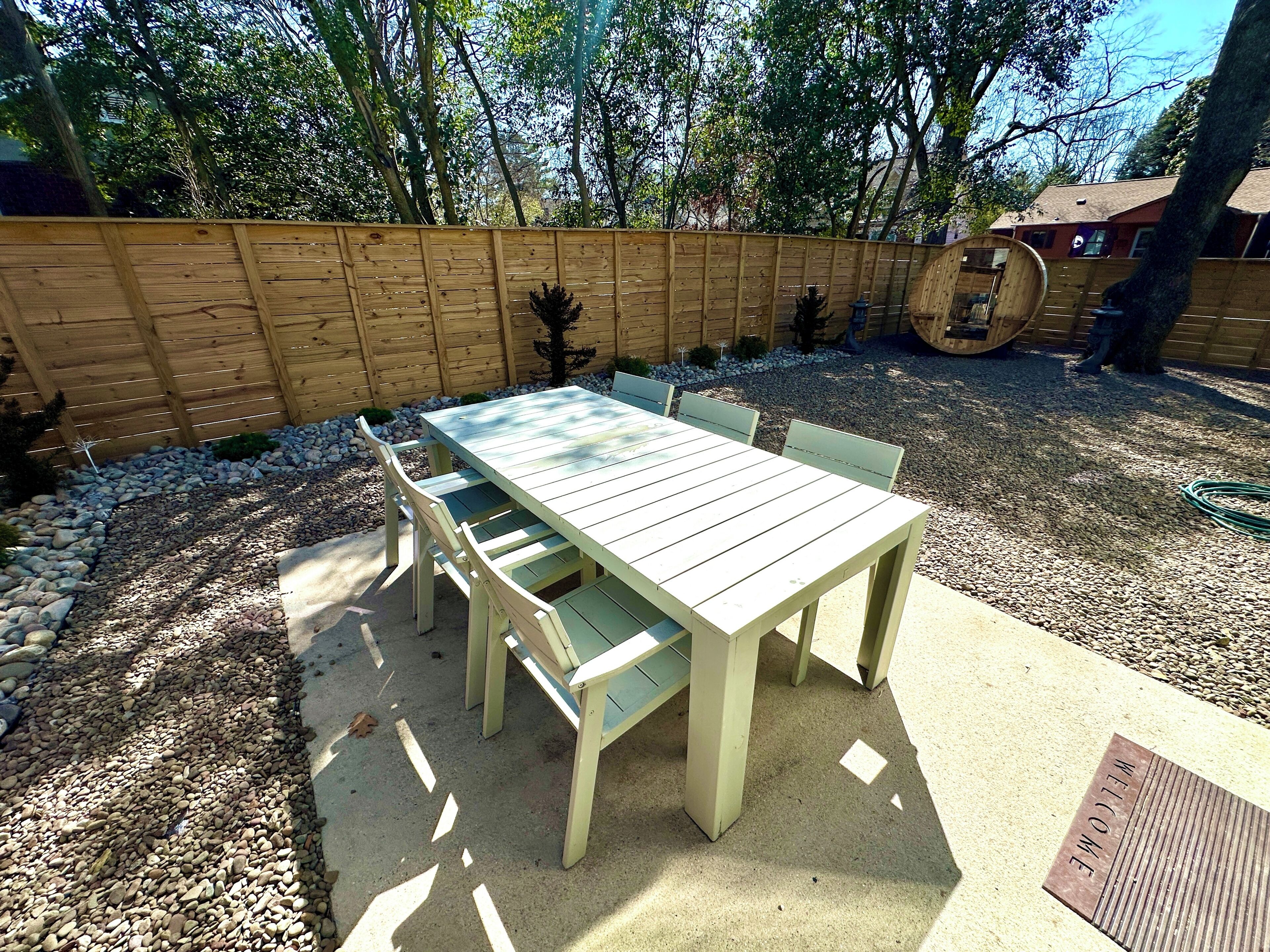 A wooden deck with a table and chairs, surrounded by a wooden fence and trees.
