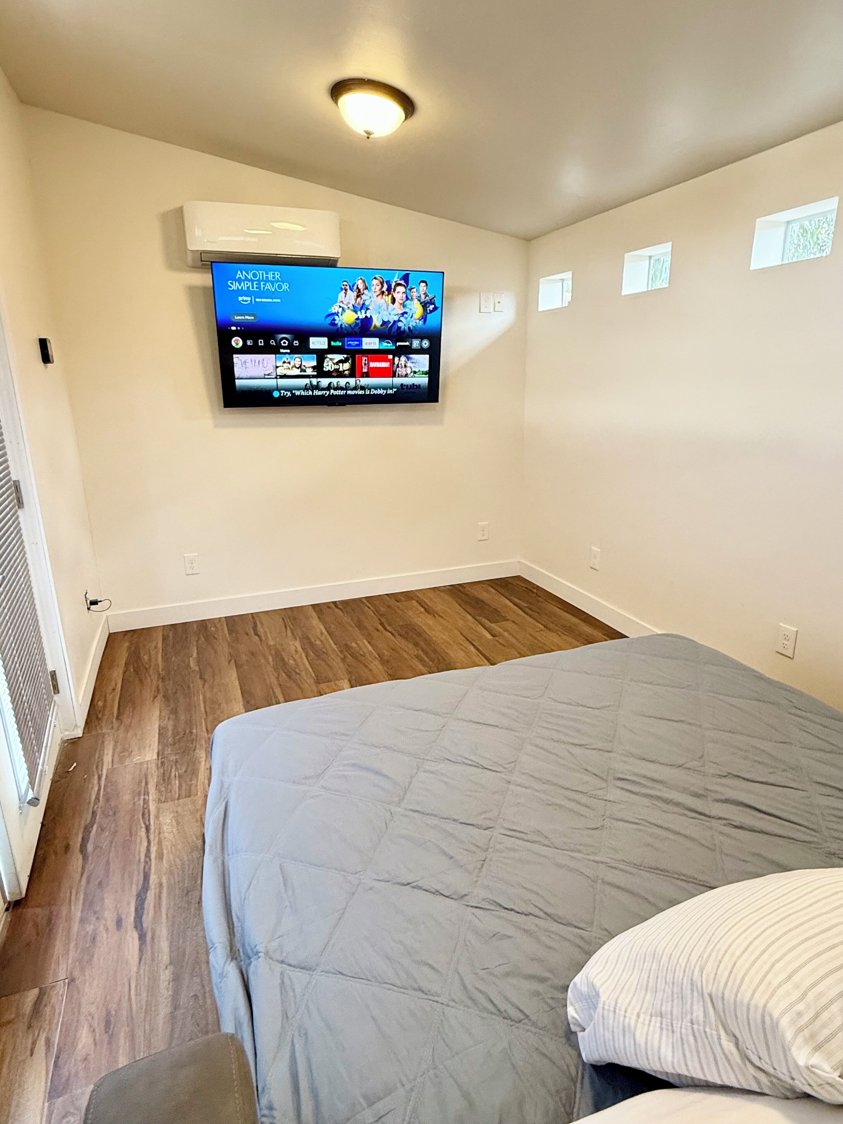 Un dormitorio con cama, un televisor de pantalla plana en la pared y una ventana.