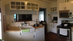 A compact kitchen with white cabinets, a microwave, a stove, and a sink. - Heritage Apartment w City and Mountain Views (North Vancouver)