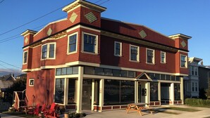 A two-story building with a red brick facade, large windows, and a covered front porch. - Heritage Apartment w City and Mountain Views (North Vancouver)