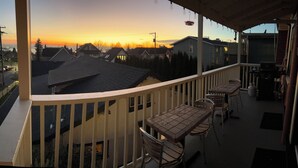 A balcony with a view of houses and a sunset. There are tables and chairs on the balcony. - Heritage Apartment w City and Mountain Views (North Vancouver)
