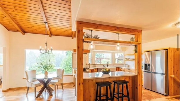 Una cucina moderna con travi in legno, un'isola centrale con sgabelli, un frigorifero e un'area pranzo con sedie e tavolo.