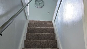 A carpeted staircase with a metal handrail, a wall clock, and a light switch.