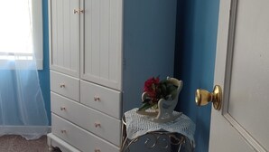 A room with a white wardrobe, a small table with a lamp, and a door with a brass doorknob.